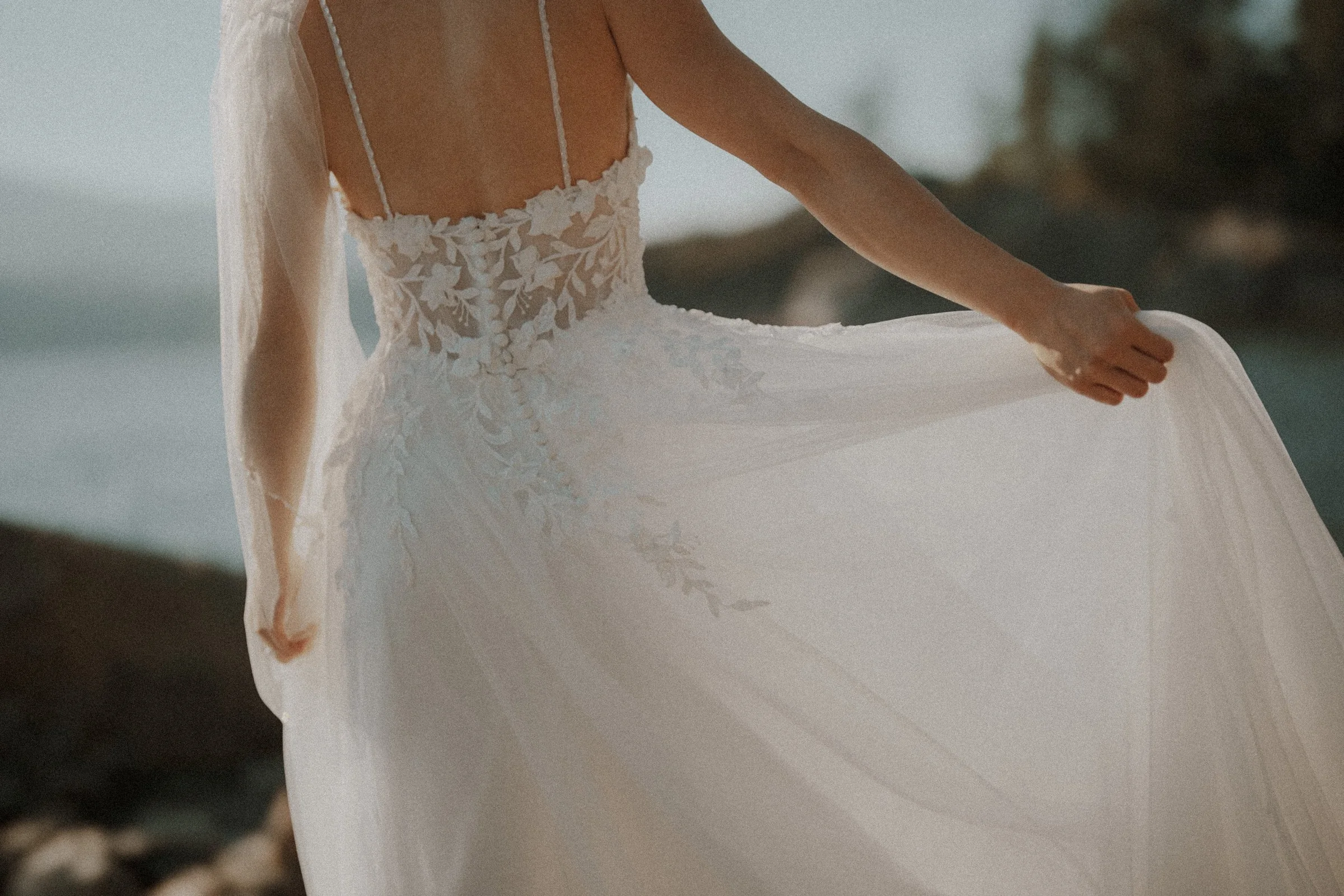 Detail of the bride's lace bodice and flowing skirt beside the coast.