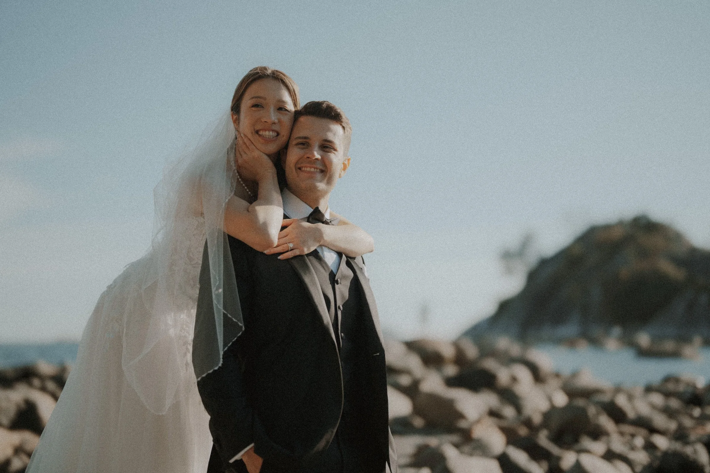 Bride and groom smiling together on the rocky Whytecliff Park shoreline.