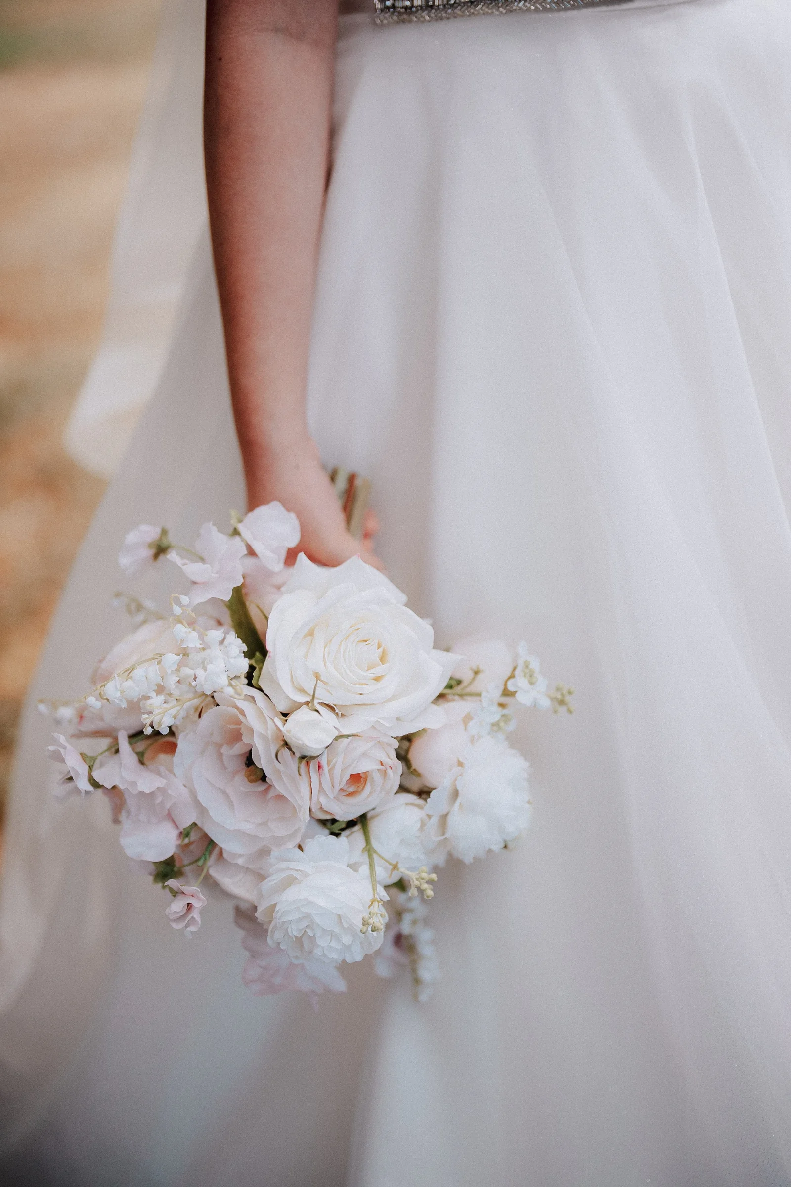 Close-up of the bride's white and pale pink bouquet beside her gown.