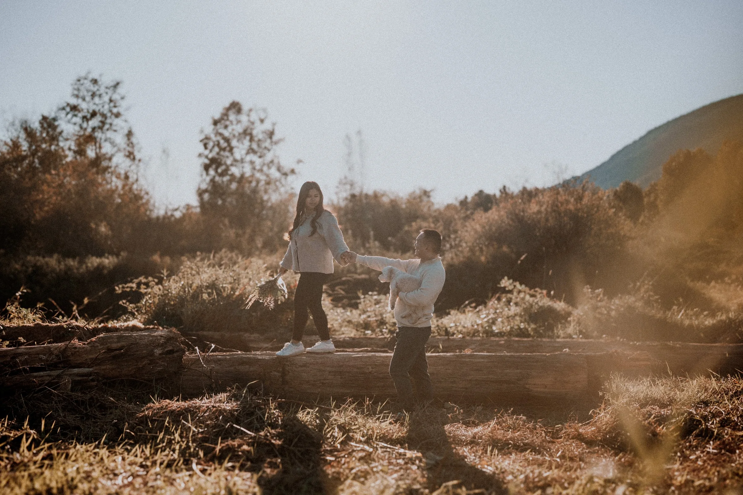 Couple walking on log holding hands, dynamic Pitt Lake adventure engagement.