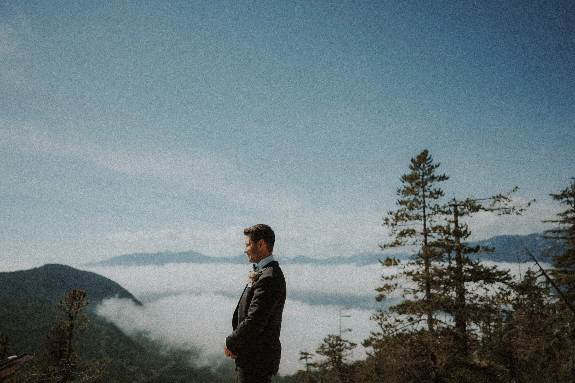 Groom standing at the mountain viewpoint above a layer of low clouds.