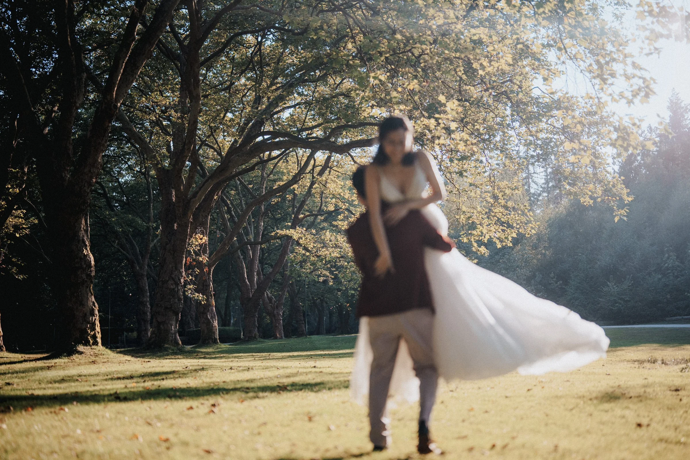Artistic candid photo of couple embracing and spinning in park, golden hour sunlight, Vancouver.