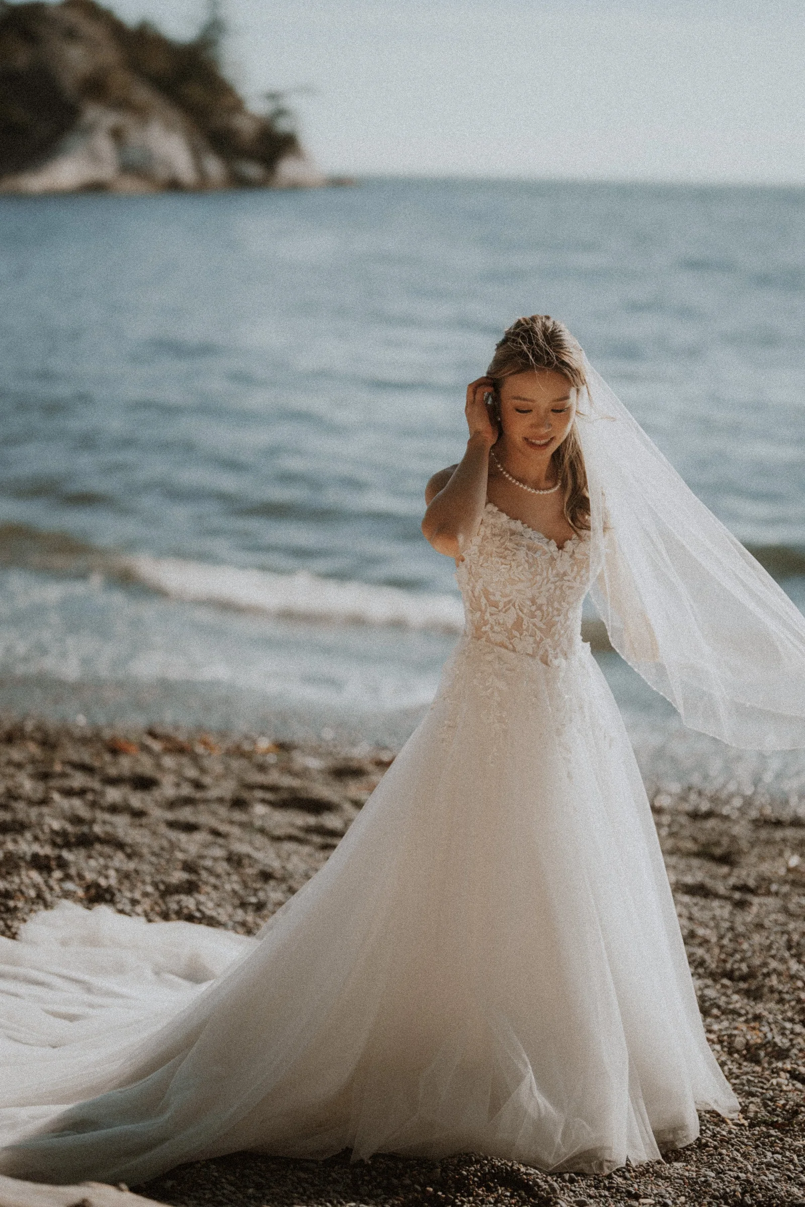 Bride arranging her gown on the Whytecliff Park shoreline.