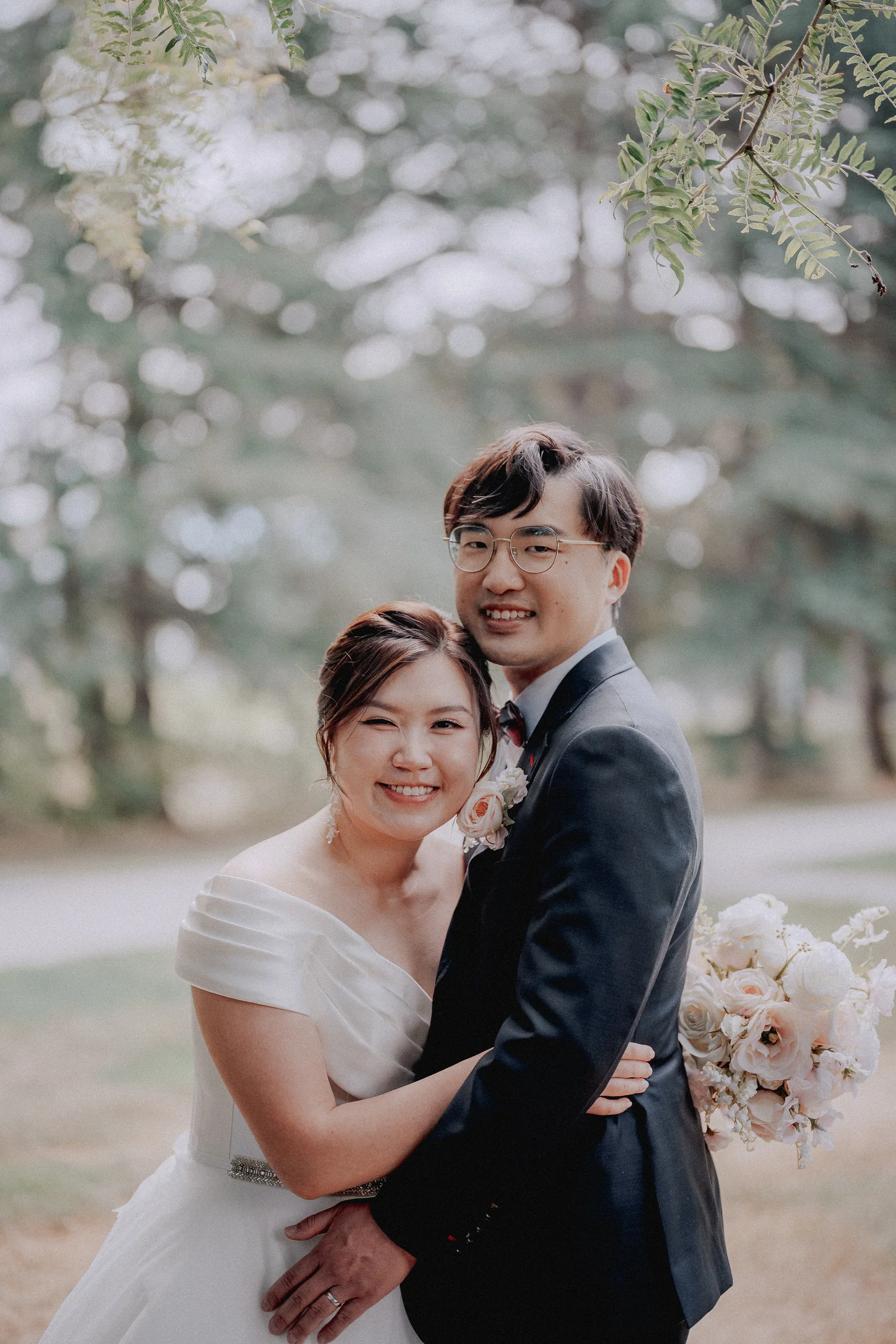 Couple embracing beneath softly lit trees in the Minoru Chapel gardens.
