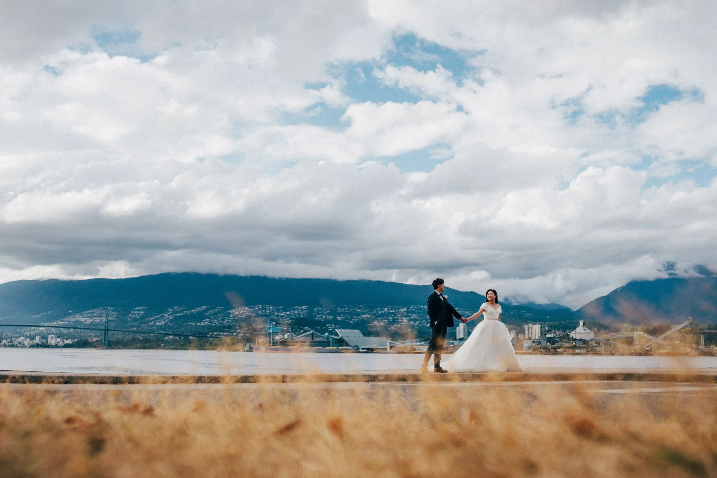 The couple walks along the water with the stunning Vancouver North Shore mountains in the distance.