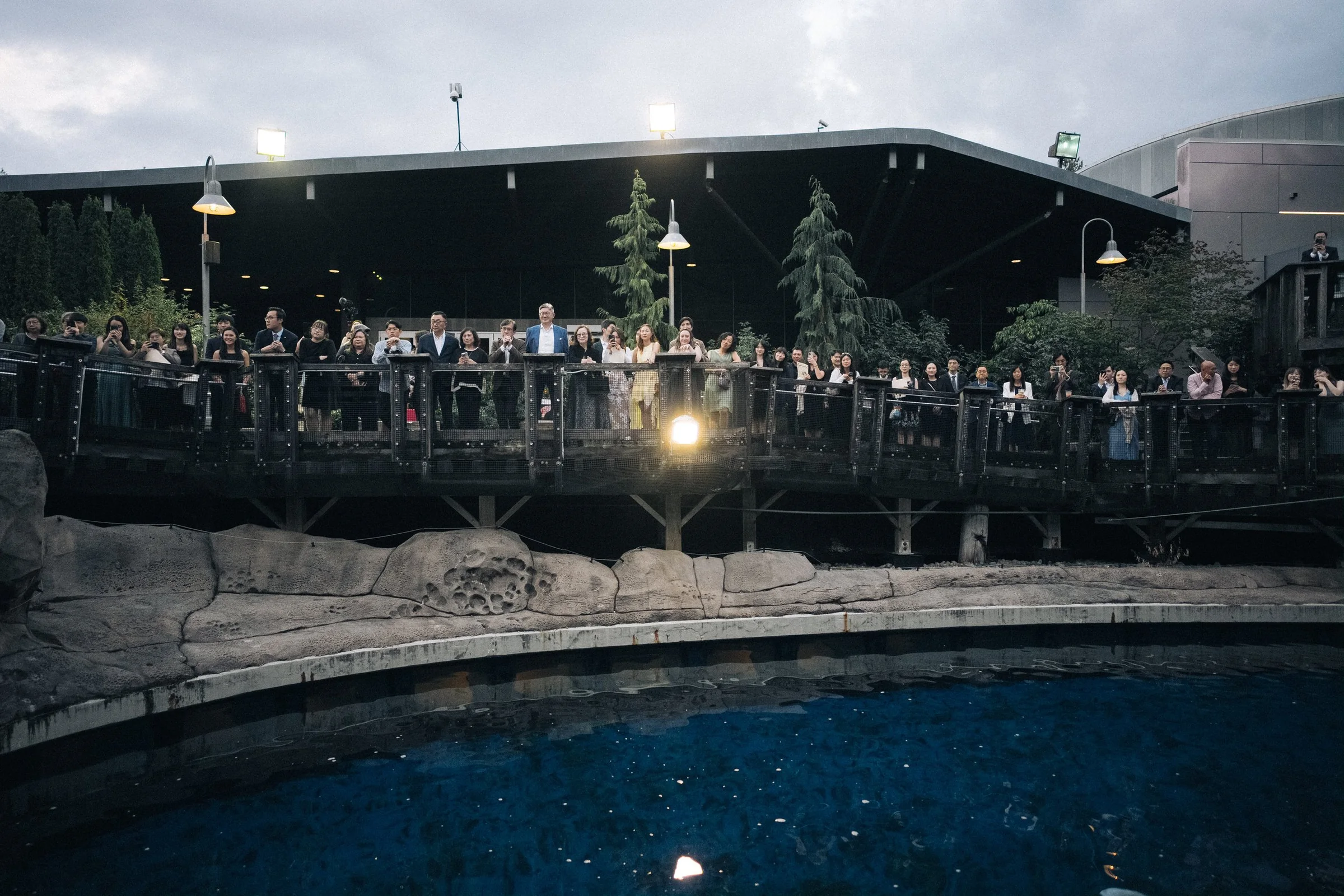 Evening view across an aquarium pool toward guests on the reception terrace.