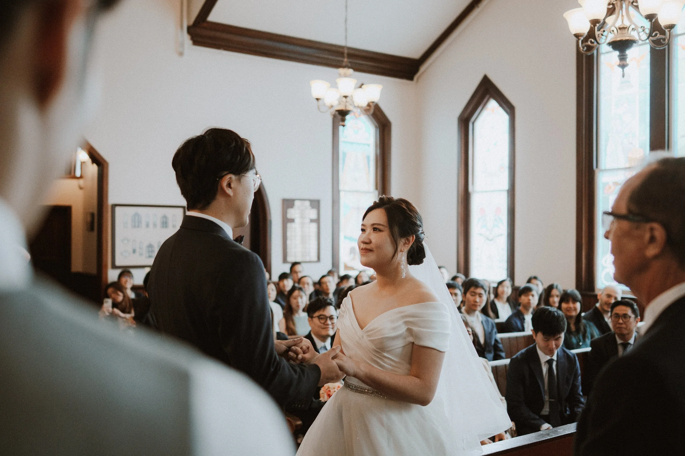 Bride speaking to the groom while guests listen from the chapel pews.
