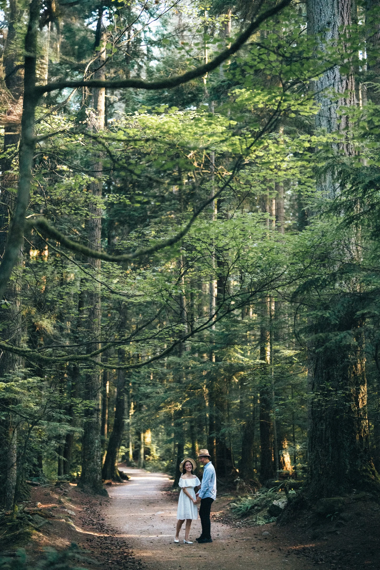 Couple standing on forest path, surrounded by tall trees, Pacific Spirit Park.