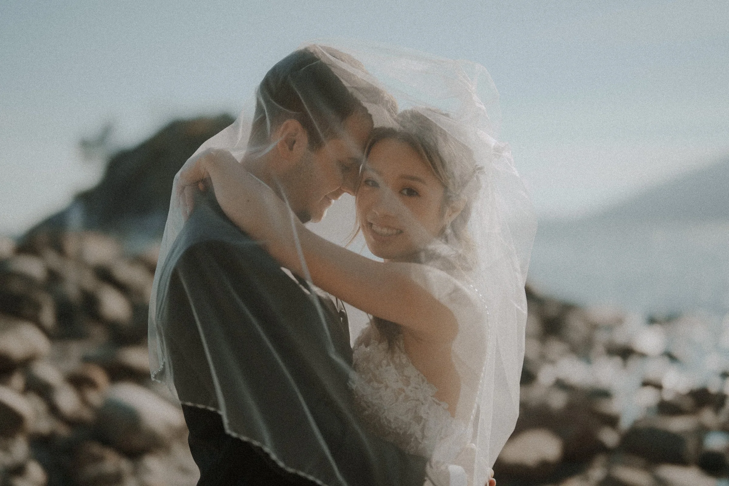 Close portrait of the bride and groom wrapped in a flowing veil.