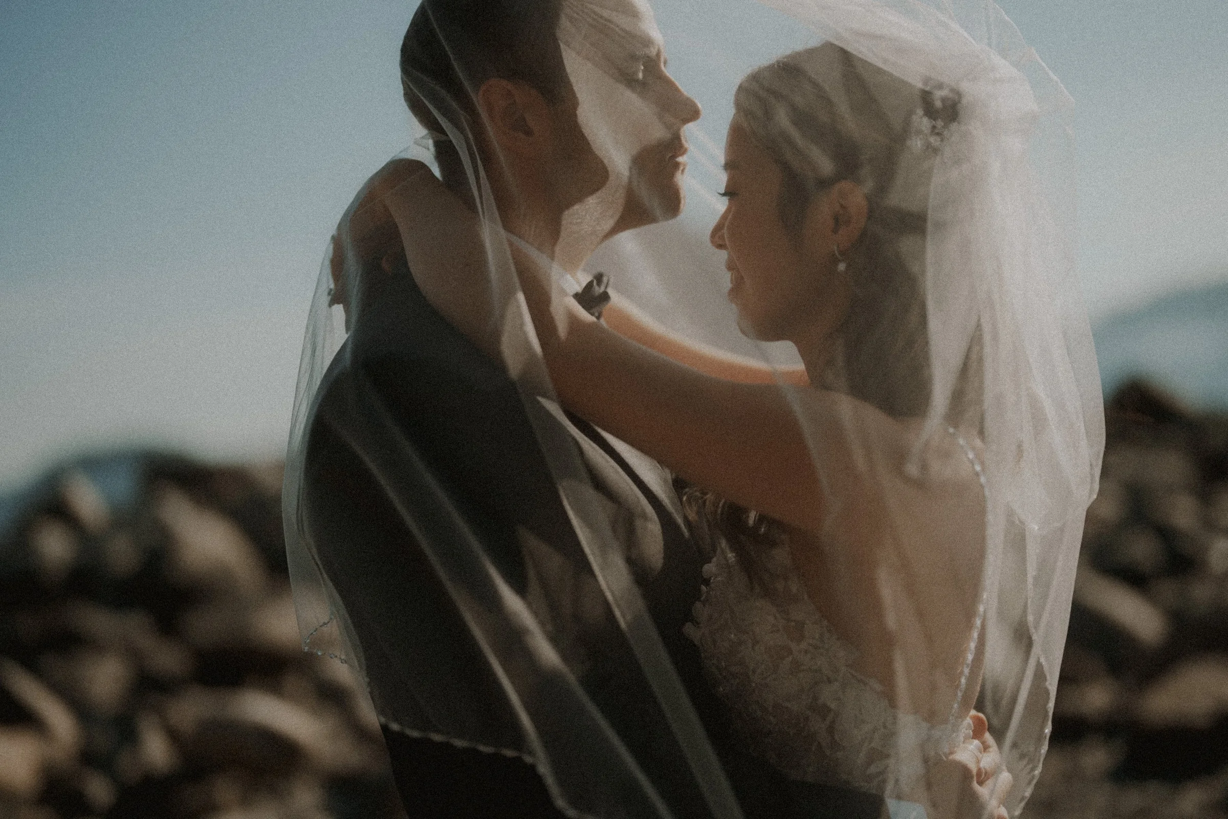 An intimate portrait of the couple embracing beneath the flowing veil, capturing the tender moment. The rugged mountain backdrop of the Sea to Sky area adds a dramatic touch.