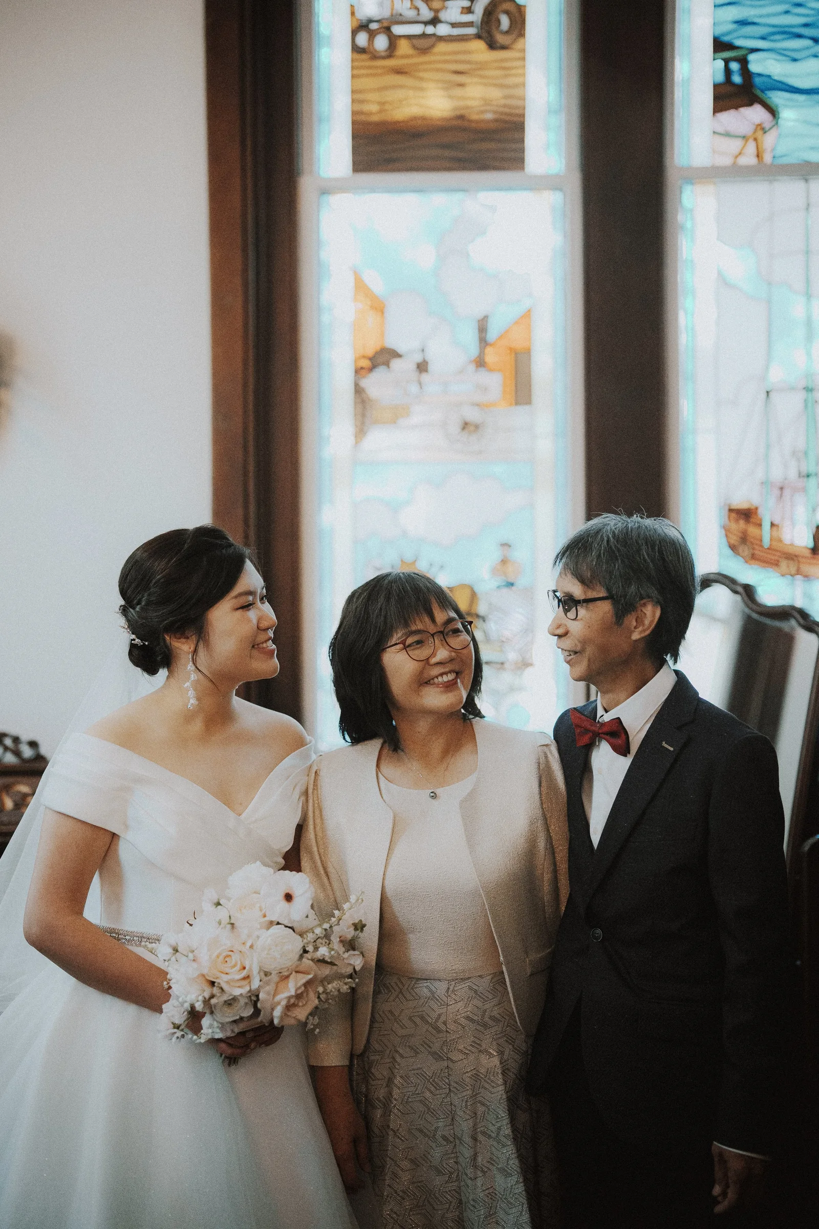 Bride with two guests beside a chapel window before her entrance.