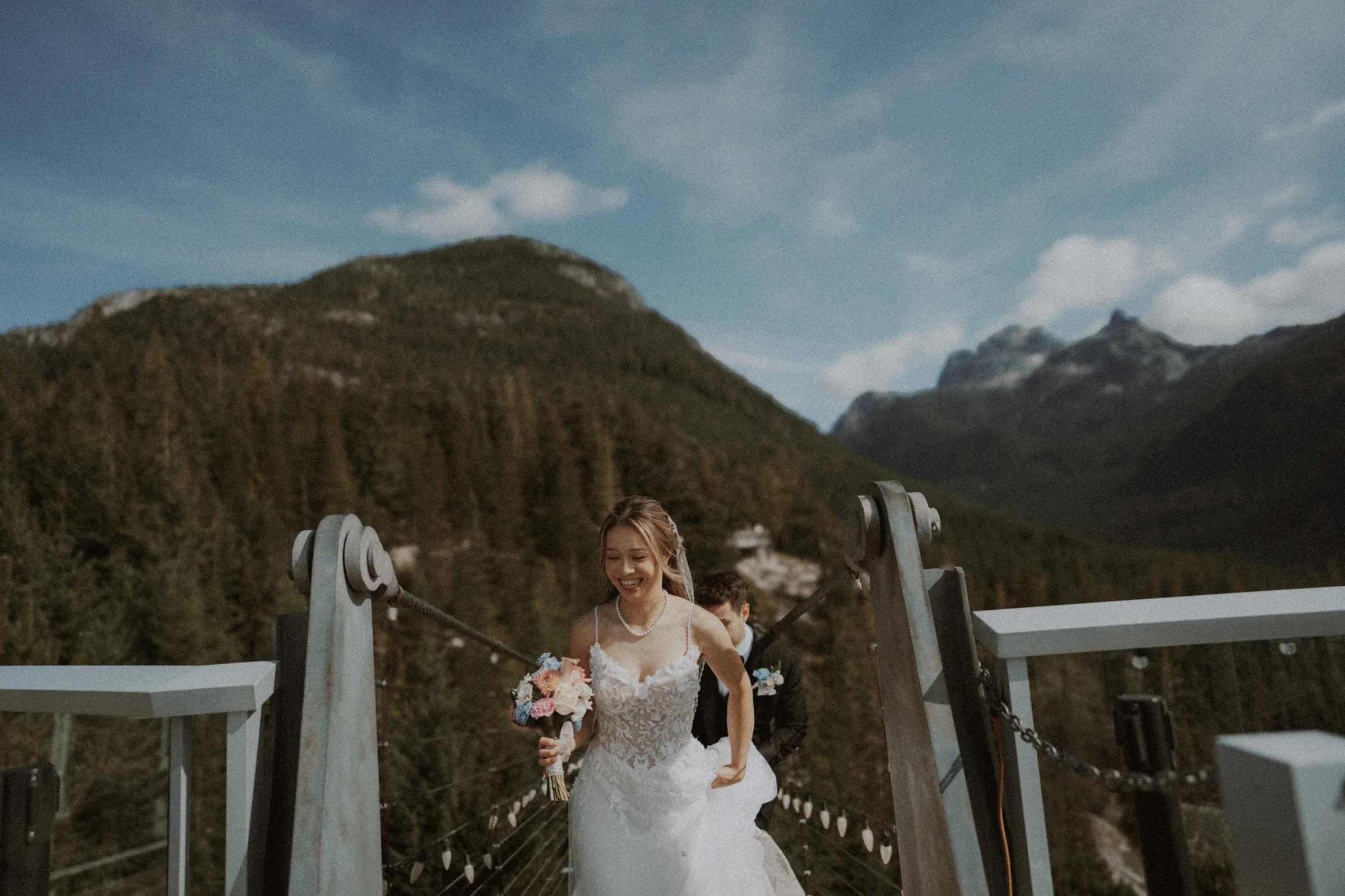 Bride stepping down from a mountain viewing platform with her bouquet.