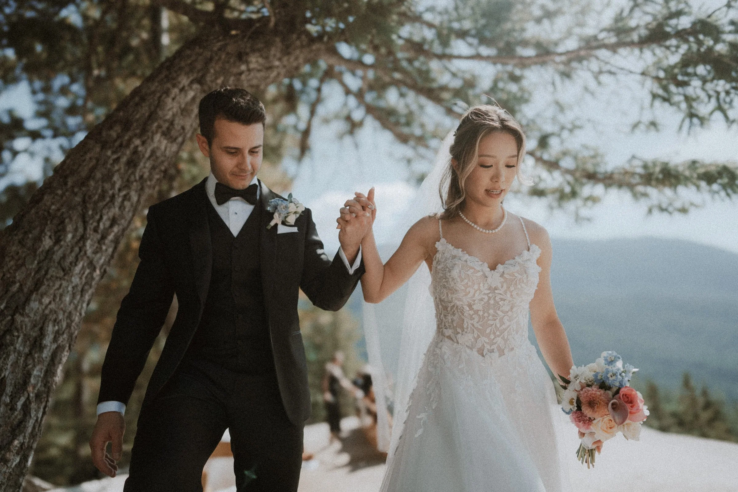 Couple holding hands on the mountain path, with the bride carrying her bouquet.