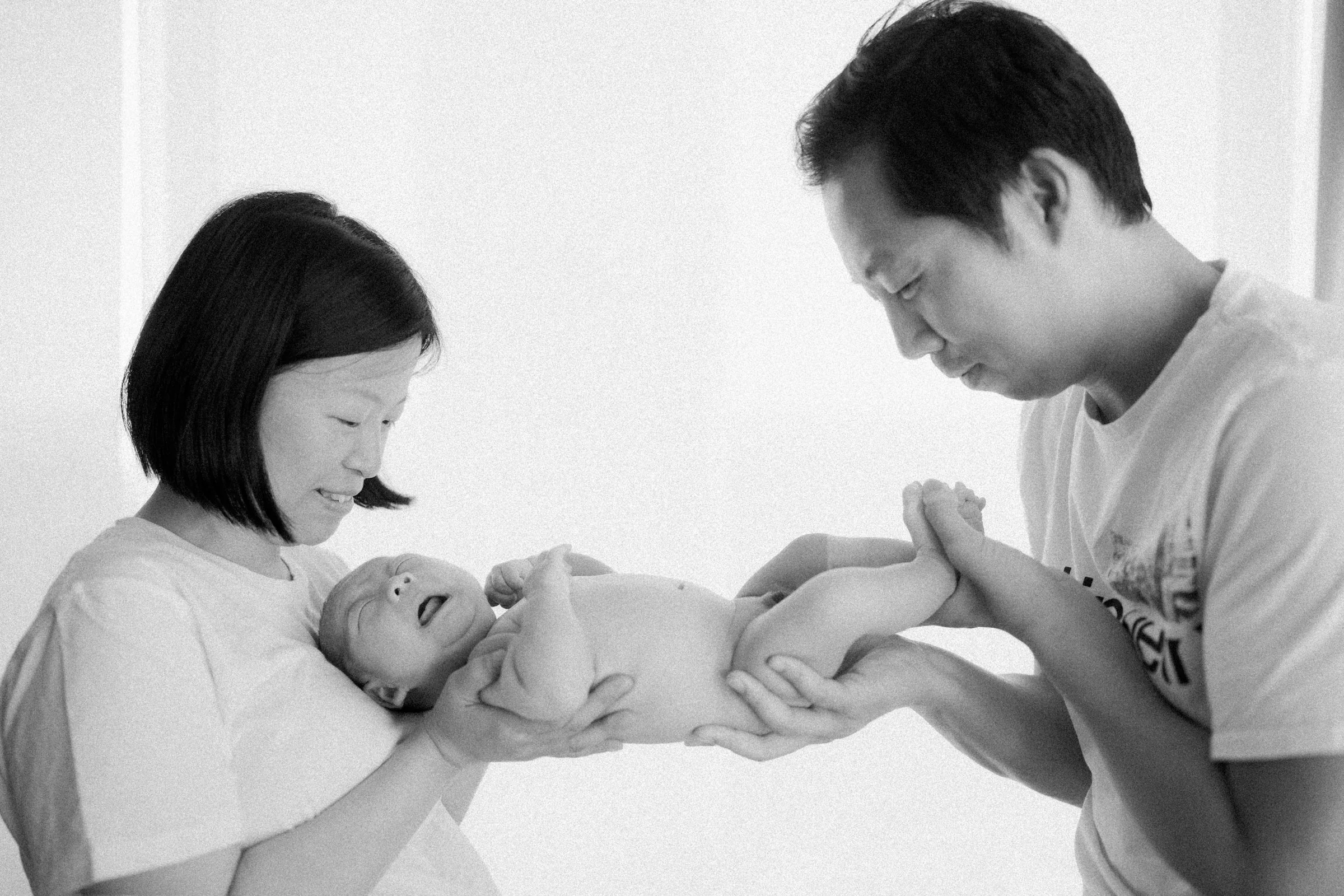 Parents holding newborn baby Apollo together, black and white lifestyle photo.