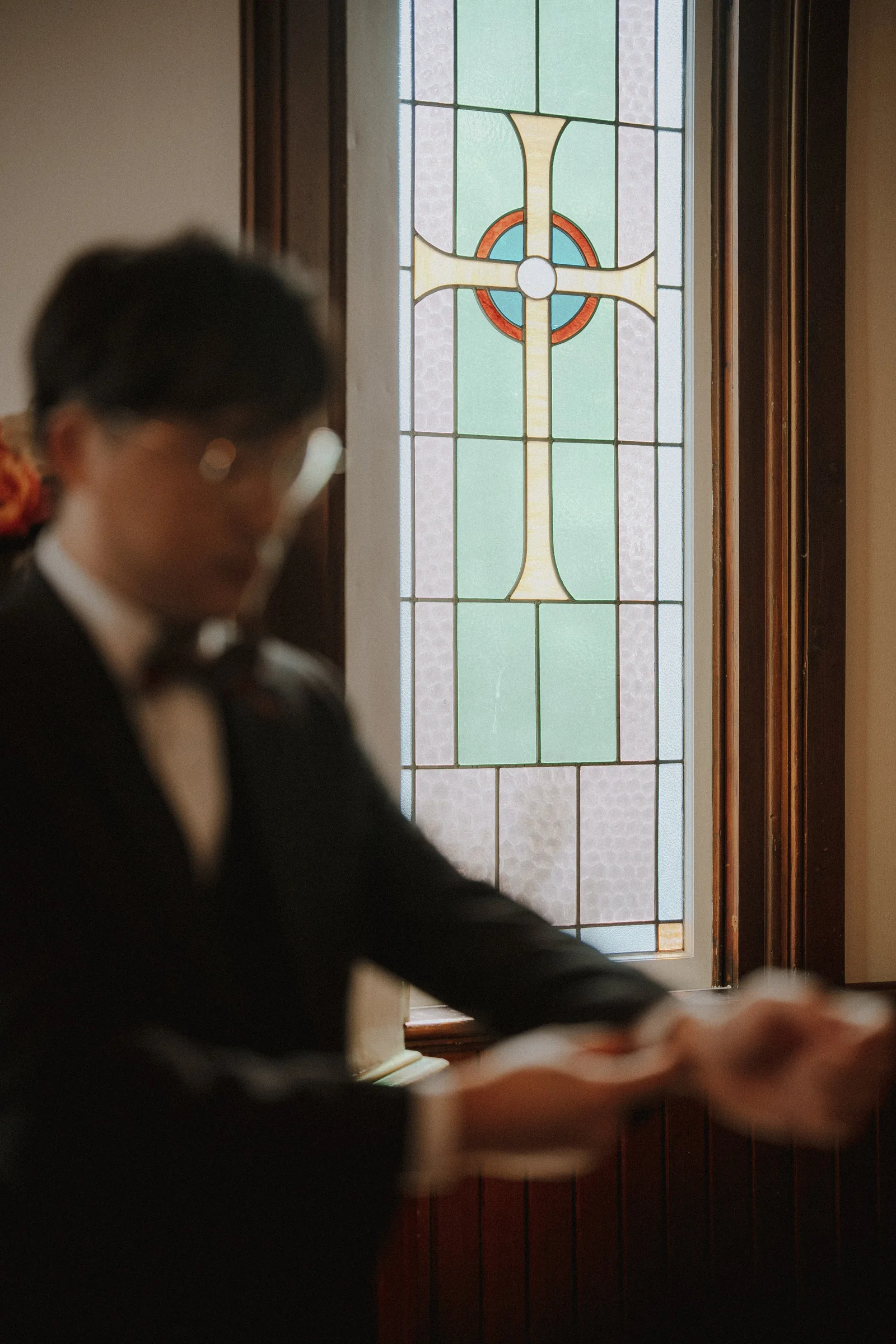 Groom adjusting his clothing beside a stained-glass window.