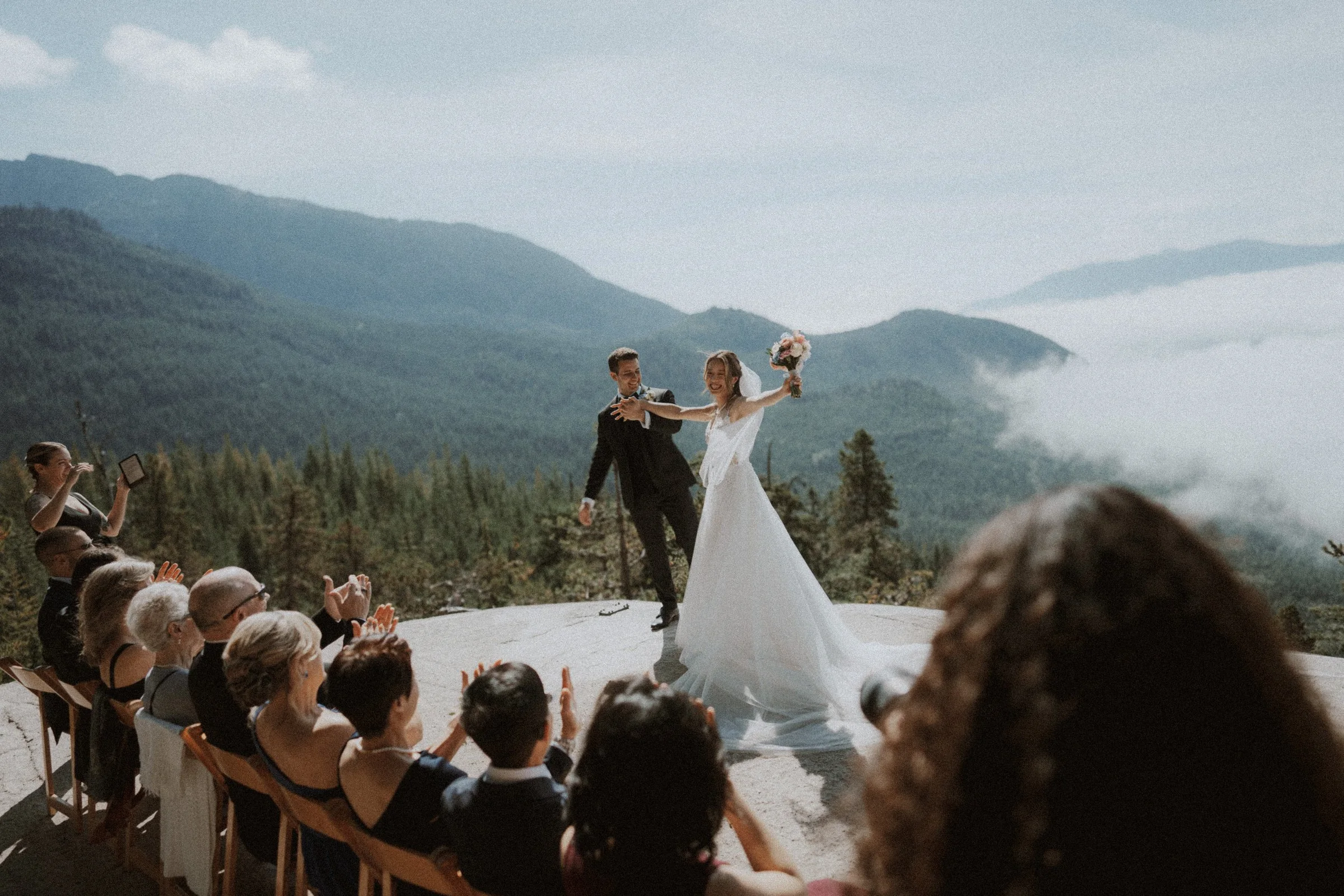 Wedding couple celebrating and cheering after ceremony, mountains and clouds in background, Sea to Sky Gondola.