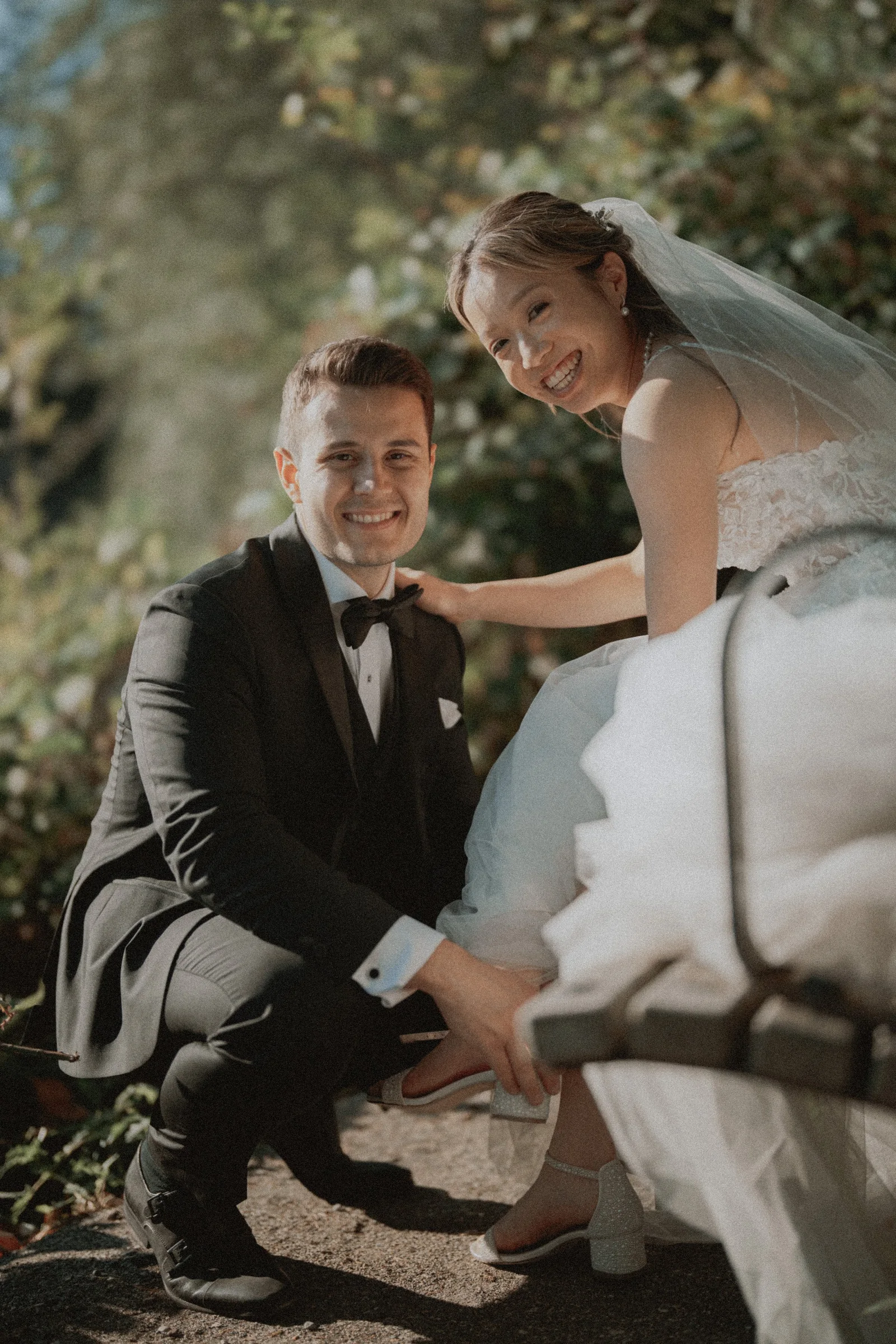 Couple smiling together beside a wooden bench on the pebbled beach.
