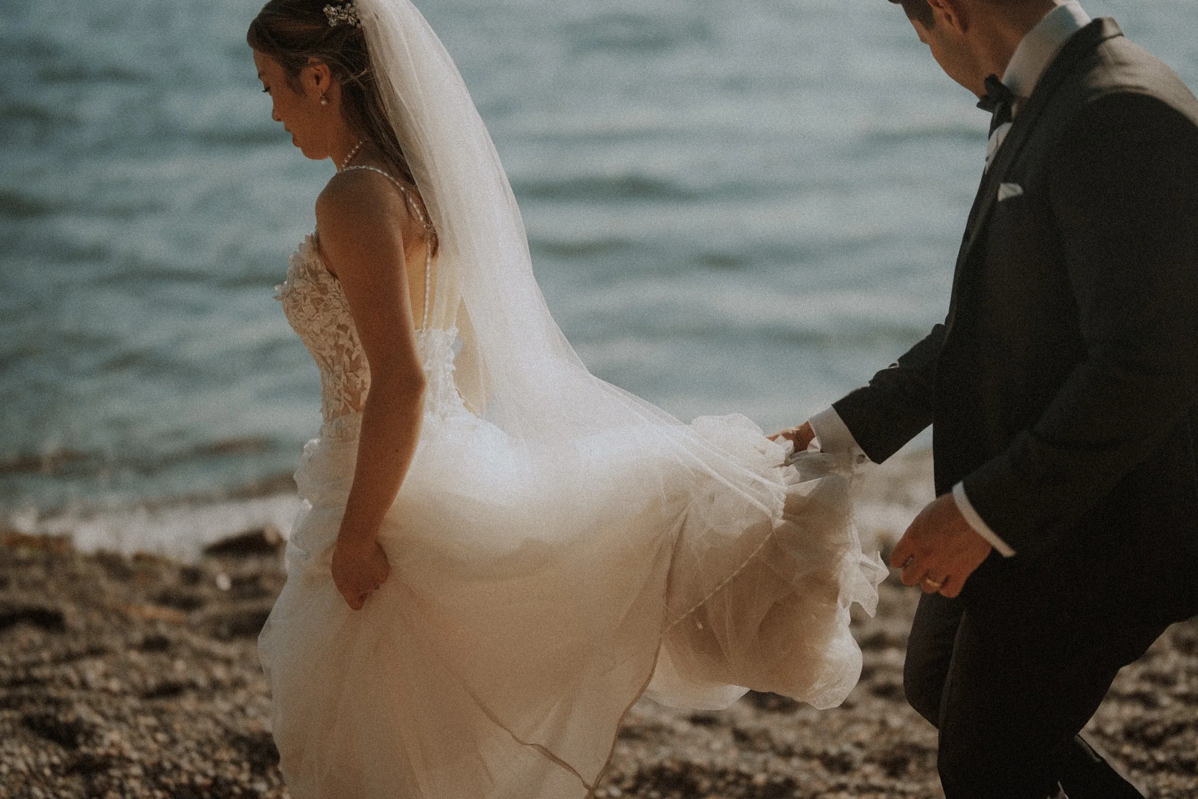 Groom lifting bride's wedding dress while walking on a beach in West Vancouver.