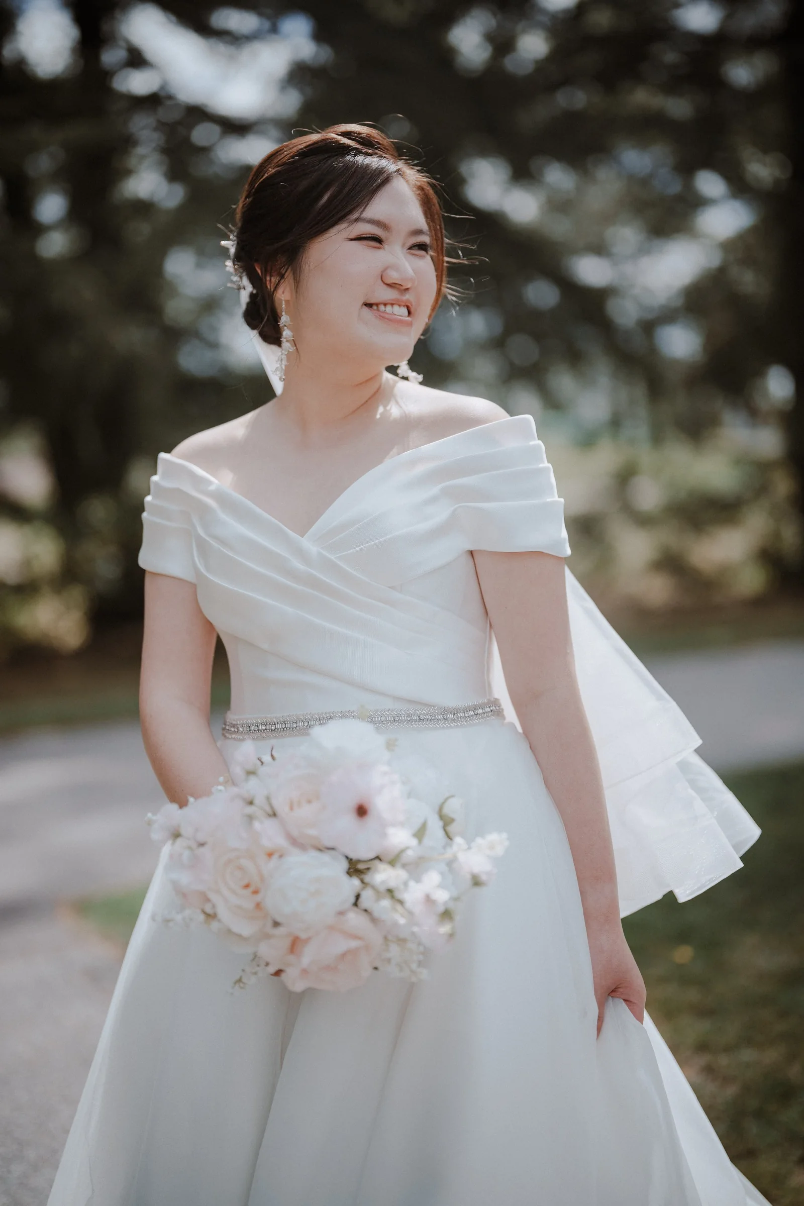 Bride portrait in natural light, smiling with off-shoulder dress and bouquet.
